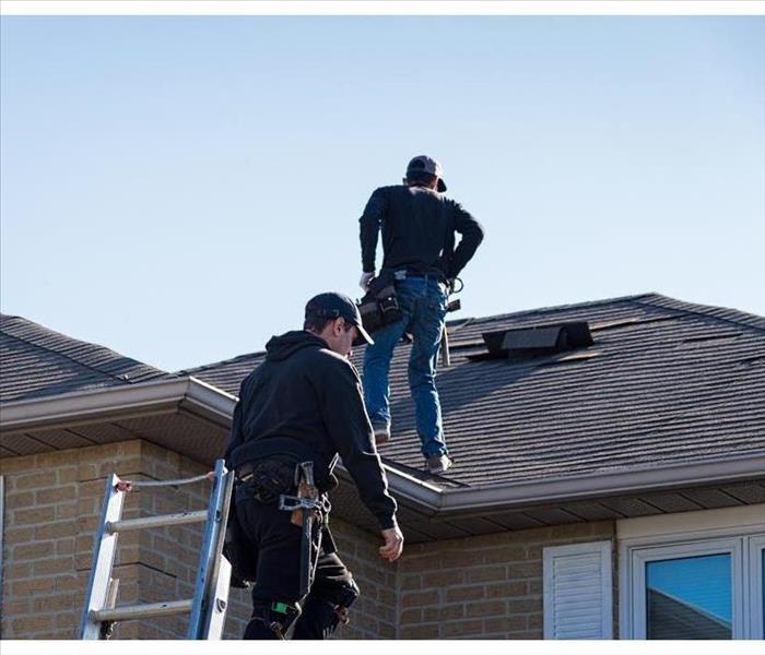 Two men on top of the roof of a house, carrying out inspection