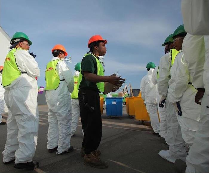 Workers in protective gear receive instructions outdoors.